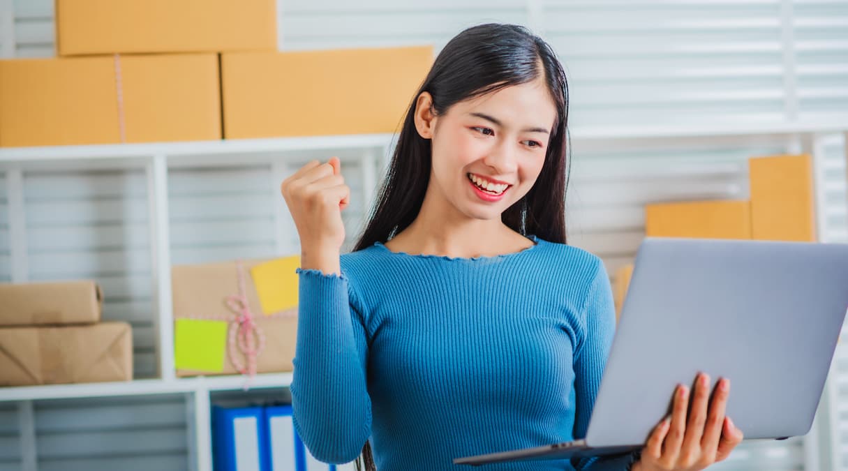 Mulher lojista trabalhando com um notebook, atrás dela há uma prateleira de produtos