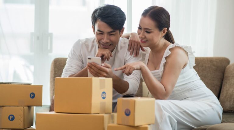 Casal de lojistas acompanhando suas vendas cercados de caixas de encomendas, um exemplo de regras de frete para loja virtual||